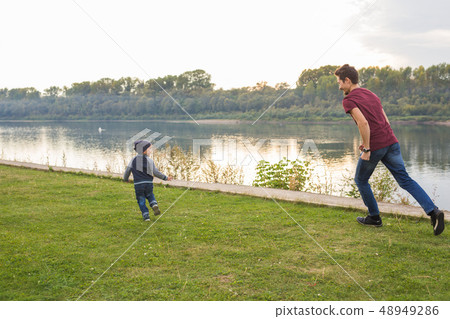 Parenthood and children concept - Father playing with a little son, trying to catch him Parenthood and children concept - Father playing with a little son, trying to catch him 48949286
