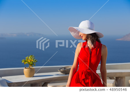 Santorini travel tourist brunette woman in red dress visiting famous white Oia village. 48950546