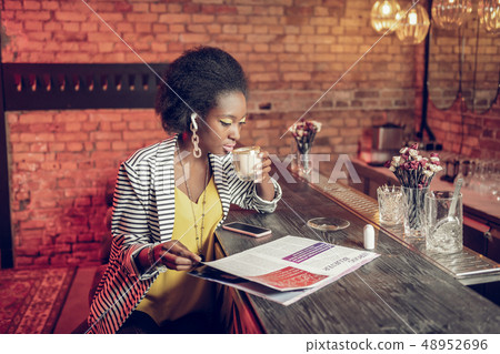 Elegant Afro-American woman drinking coffee and flipping fashion magazine 48952696