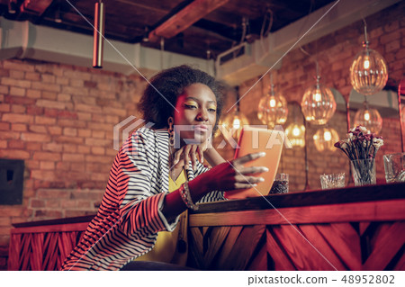 Concentrated Afro-American female watching video on tablet sitting at bar Concentrated Afro-American female watching video on tablet sitting at bar 48952802