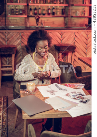 Smiling African lady doing fashion design drawing sitting in cafeteria. Smiling African lady doing fashion design drawing sitting in cafeteria. 48953215