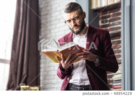 Stylish handsome man standing near window while reading book 48954229