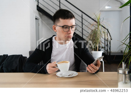 Worried young man reading a message with bad notification on modern smartphone sitting in cafe Worried young man reading a message with bad notification on modern smartphone sitting in cafe 48962253