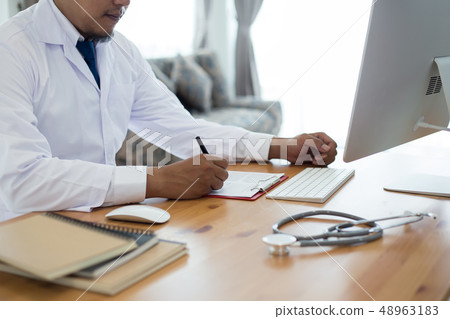 doctor sits  in the clinic writing  a prescription 48963183