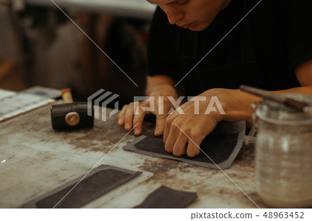 Close up of leather craftsman working with natural leather. Handmade master at work in local 48963452