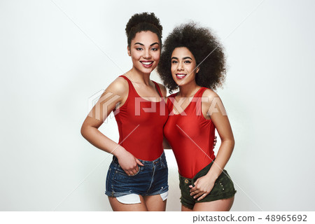 Looking amazing! Two attractive afro american women looking at camera and smiling while standing Looking amazing! Two attractive afro american women looking at camera and smiling while standing 48965692