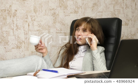 woman in office drinking coffee resting in workplace. beautiful businesswoman with phone sits in a woman in office drinking coffee resting in workplace. beautiful businesswoman with phone sits in a 48966924