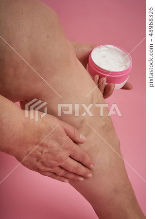 Senior woman applies cream on legs with varicose veins on coral background. 48968326
