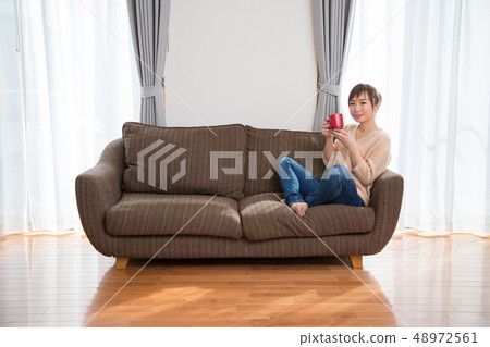 Woman sitting on a couch and drinking a drink 48972561