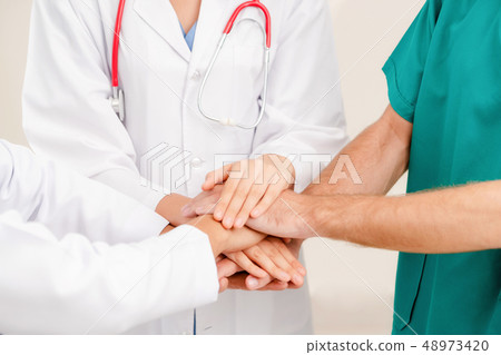 Doctor, surgeon and nurse join hands together. 48973420