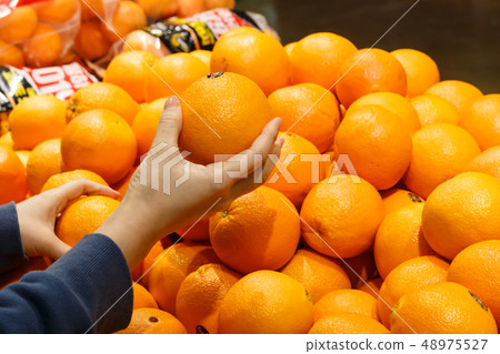 A housewife's hand picking oranges from a large mart fruit corner 48975527