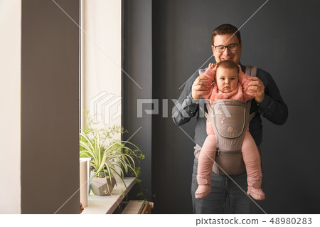 Fathre and his kid in baby carrier at the grey background wall, baby wearing concept Fathre and his kid in baby carrier at the grey background wall, baby wearing concept 48980283