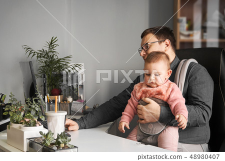 Man father with baby in carrier working at office or home with computer at the desk, parent in 48980407