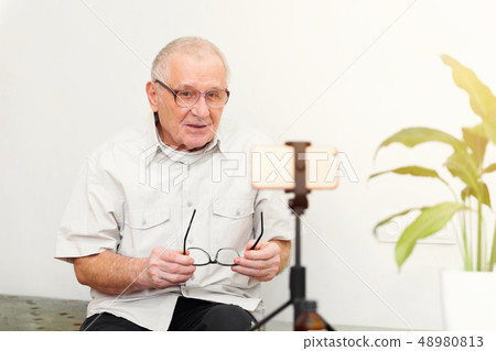Smiling eldery man looking at camera making video blog or call at home sitting on sofa dating online 48980813
