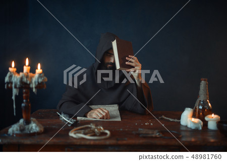 Medieval monk sitting at the table and reads 48981760