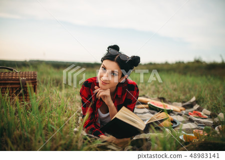 Woman with book lies on plaid, picnic in field 48983141