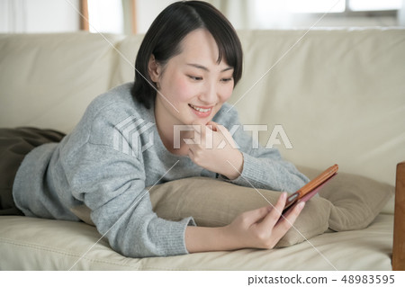 說謊在沙發和觀看智能手機的一名年輕日本婦女 48983595