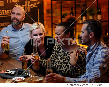 Group of friends watching tv in a cafe behind bar counter Group of friends watching tv in a cafe behind bar counter 48988409