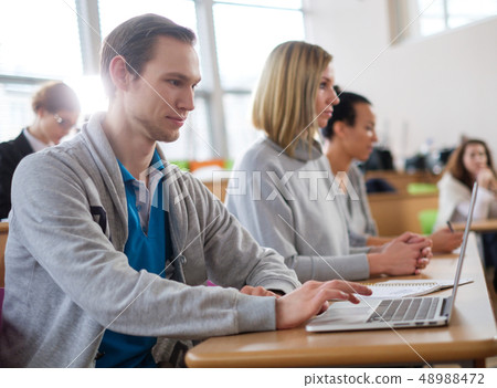 Man with laptop among students in an auditorium Man with laptop among students in an auditorium 48988472