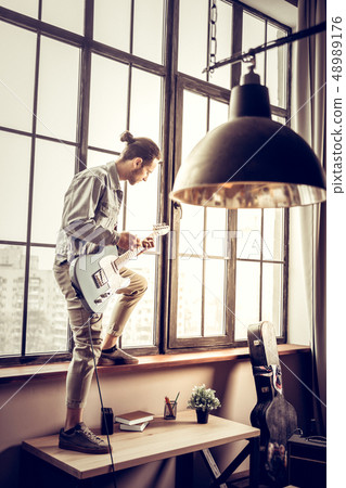 Rock musician standing on table near window and playing the guitar 48989176