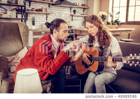 Music tutor teaching girl to move fingers while playing the guitar 48989598