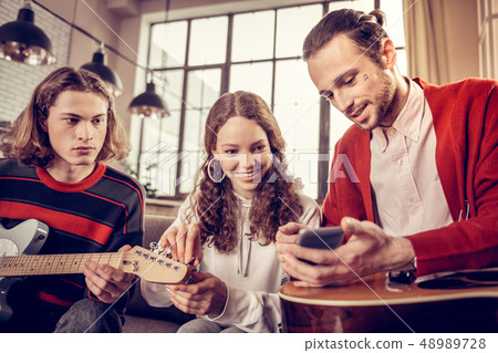 Beaming curly girl feeling joyful while learning to play guitar 48989728