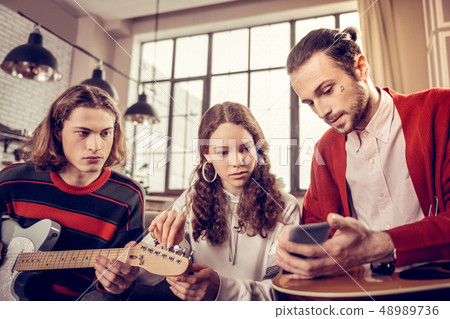 Bearded guitar tutor holding his phone and showing musical notes Bearded guitar tutor holding his phone and showing musical notes 48989736