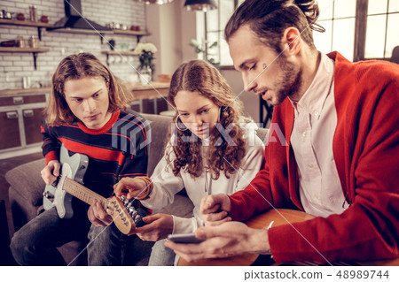 Guitar tutor with little tattoo on his face teaching brother and sister 48989744