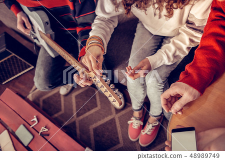 Top view of curly girl trying to tune the guitar sitting near friends Top view of curly girl trying to tune the guitar sitting near friends 48989749