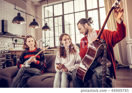 Teenage girl spending time with her brothers playing the guitar Teenage girl spending time with her brothers playing the guitar 48989785