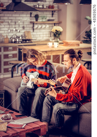Participants of band sitting on sofa and playing music instruments 48989876