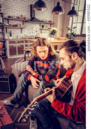 Man striped sweater listening to his friend playing the guitar Man striped sweater listening to his friend playing the guitar 48990502
