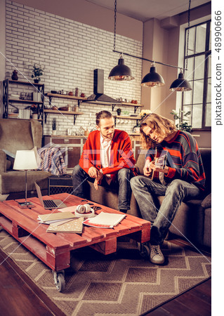Student wearing jeans and sweater playing the guitar near tutor 48990666