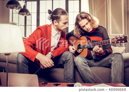 Bearded dark-haired guitar teacher listening to his student Bearded dark-haired guitar teacher listening to his student 48990669