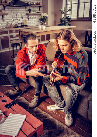 Men wearing jeans sitting on sofa and composing new song 48990718