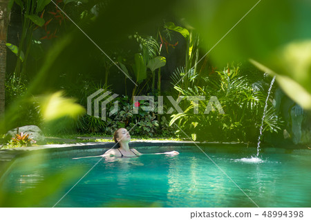 Sensual young woman relaxing in outdoor spa infinity swimming pool surrounded with lush tropical Sensual young woman relaxing in outdoor spa infinity swimming pool surrounded with lush tropical 48994398