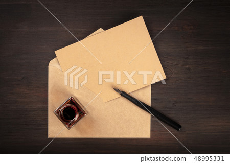 An overhead photo of an ink well with a brown craft card in an envelope, with an ink pen and copy An overhead photo of an ink well with a brown craft card in an envelope, with an ink pen and copy 48995331