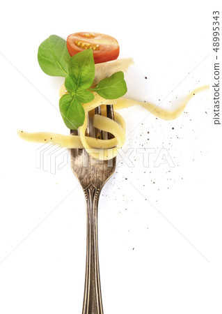 Italian pasta. Overhead photo of vintage fork with pappardelle, basil, cheese, and tomato, on white 48995343