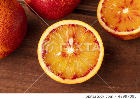 A closeup photo of an organic blood orange on a dark rustic wooden background with copy space 48997093