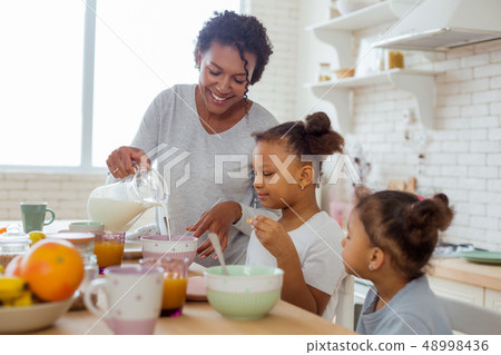 Cheerful young woman pouring down milk into bowl 48998436