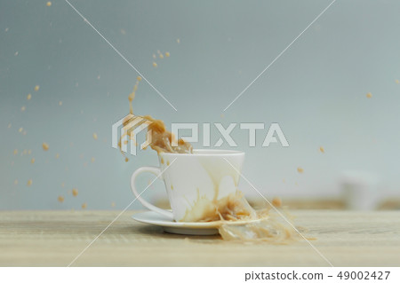 Splash in white cup of coffee on wooden table Splash in white cup of coffee on wooden table 49002427