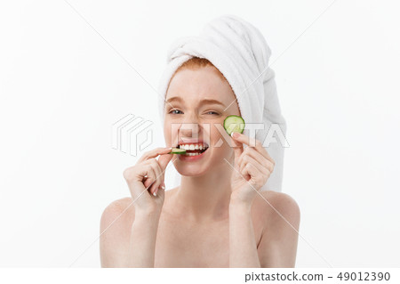 Attractive Young Woman with beautiful clean skin. White mask and cucumbers. Beauty treatments and 49012390