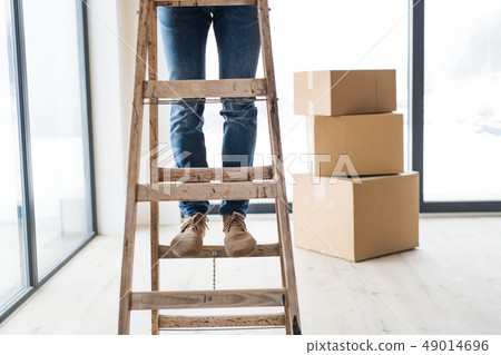 A midsection of man with cardboard boxes standing on a ladder, furnishing new house. 49014696