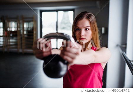 A portrait of young girl or woman doing exercise with a kettlebell in a gym. A portrait of young girl or woman doing exercise with a kettlebell in a gym. 49014741