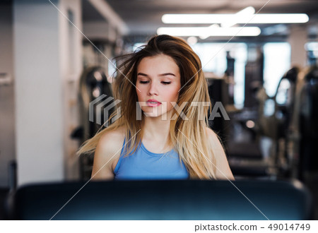 A portrait of young girl or woman doing cardio workout in a gym. A portrait of young girl or woman doing cardio workout in a gym. 49014749