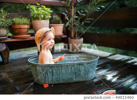 Small boy with a hat in bath outdoors in garden in summer, eating watermelon. Small boy with a hat in bath outdoors in garden in summer, eating watermelon. 49015460