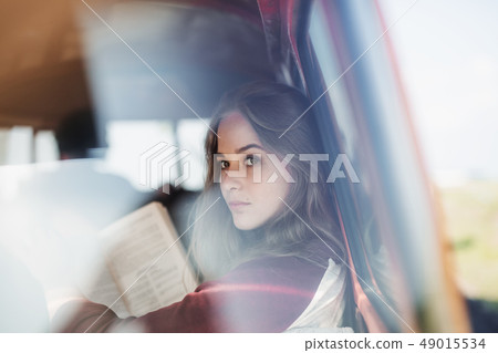 A group of young friends on a roadtrip through countryside, a girl reading a book. 49015534