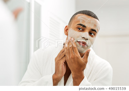 Man looking in the mirror with white clay mask  49015539