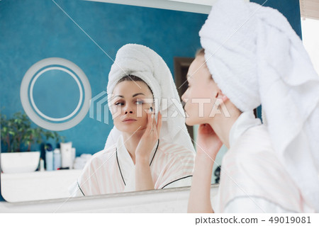 Young woman looking at camera and applying cream Young woman looking at camera and applying cream 49019081