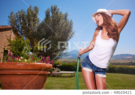 Happy sexy woman watering flowers in italy garden 49020421